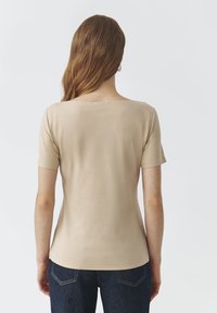 Haut beige à manches courtes avec une texture lisse, encolure ronde et coupe ajustée, associé à un jean en denim foncé.