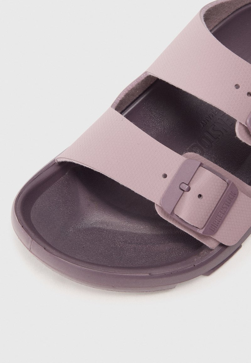 Sandale en caoutchouc violet avec deux brides réglables. Tige texturée et semelle intérieure lisse. Comprend une boucle et un logo de marque en relief sur la bride.