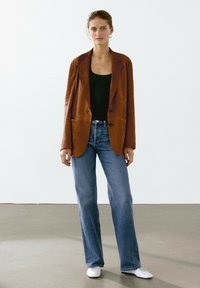 Brun mocka blazer med kavajslag, ihop med en svart ribbad linne och ljusblå utsvängda jeans. Stylad med vita skor.