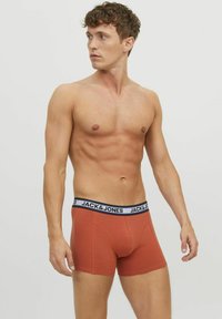 Boxer cortos en color naranja quemado con una cinturilla negra etiquetada "JACK & JONES". Tejido suave con un acabado liso, diseño ajustado.