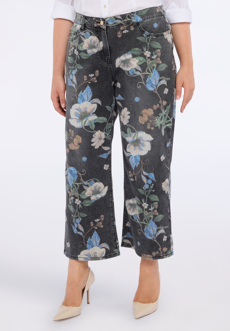 Jeanși negri scurți cu un imprimeu floral mare în nuanțe de albastru și bej, purtați cu pantofi cu toc înalt bej și o cămașă albă cu mânecile suflecate.