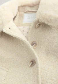 Beige strukturierten Mantel mit einem Kunstfellkragen, Knopfverschlüssen und einem floral gemusterten Futter. Das Material wirkt weich und gemütlich.