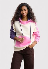 Bluza z kapturem w kolorach kremowym, różowym i fioletowym. Posiada dużą przednią kieszeń, sznurki oraz ściągacze przy rękawach. Miękka tkanina o luźnym kroju.
