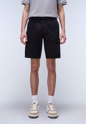 Black cargo shorts with two side pockets, made from cotton fabric, featuring a regular fit and a button closure, paired with beige sneakers.