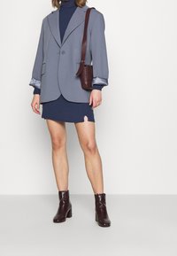 Šedý blazer s jedním knoflíkem, oversized rukávy s saténovým manžetem, v kombinaci s námořnickým šaty a bordó lodičkami.