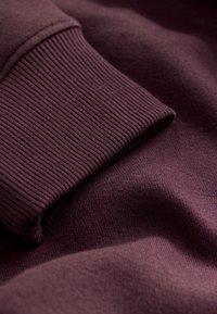 Mörklila sweatshirt-tyg med ribbad mudd och slät textur, delvis vikt för att visa materialets mjukhet och rikedom.