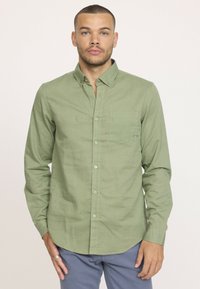 Chemise verte à manches longues avec boutons en tissu léger, dotée d'une poche poitrine et d'un col classique, avec une texture lisse et une finition douce.