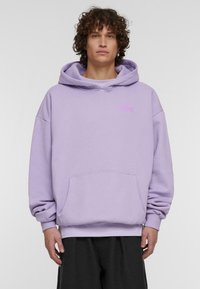 Vijolična kapuca z vrvico, velikim sprednjim žepom in mehkimi tkaninami. Ima majhen roza logotip na prsih.