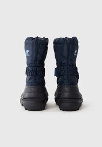 Par de botas de invierno aisladas en azul marino con suelas de goma negras y correas de velcro elásticas, vistas desde atrás sobre un fondo gris.