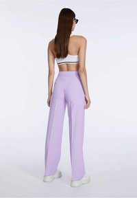 Lila wijde broek met hoge taille, gemaakt van een gladde stof en met een relaxte pasvorm, gecombineerd met een witte crop top en witte sneakers.