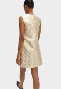 Vestido sin mangas de metal dorado con superficie texturizada; forma A-line; cierre de cremallera en la parte posterior; acabado suave; longitud por encima de la rodilla.