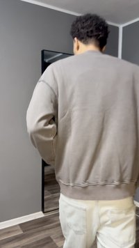 Sweat-shirt gris avec poignets et ourlet côtelés, associé à un pantalon de couleur claire. En arrière-plan, un miroir et des tons neutres sur les murs.