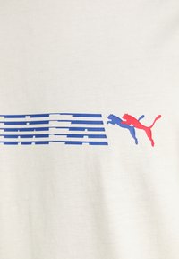 Balta medvilninė marškinėliai su mėlyna ir raudona grafika, horizontaliais dryžiais ir dviem šokliškais puma dešinėje pusėje.