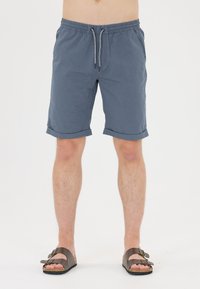 Blå, lätta, knälånga shorts med dragsko i midjan och uppvikta f�ållar. Bärs med bruna sandaler med två remmar på bara ben.