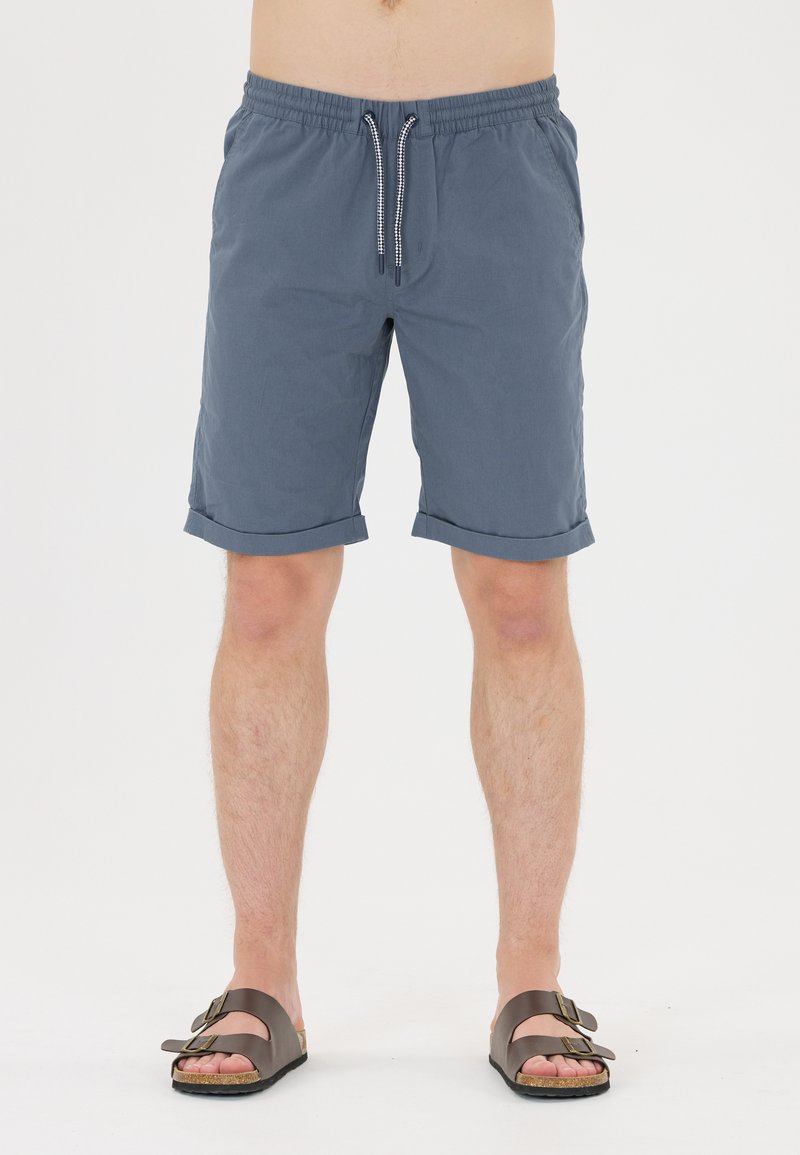 Blå, lätta, knälånga shorts med dragsko i midjan och uppvikta fållar. Bärs med bruna sandaler med två remmar på bara ben.