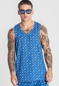 Modré tielko s opakujúcim sa vzorom loga, vyrobené z jemnej tkaniny. Dizajn obsahuje široké ramienka a okrúhly výstrih.