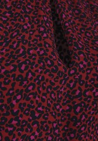 Red fabric with dense black and purple leopard print pattern, slightly gathered or folded.