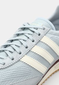 Αθλητικό παπούτσι σε ανοιχτό μπλε χρώμα με υφασμάτινη δαντελένια επάνω επιφάνεια, σουέτ λεπτομέρειες, τρεις λευκές ρίγες και καφέ λάστιχο σόλα.