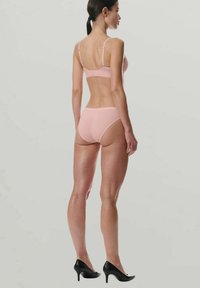 Lichtroze beha en bijpassende slip van zacht materiaal, met verstelbare bandjes en een eenvoudig ontwerp, gecombineerd met zwarte pumps.