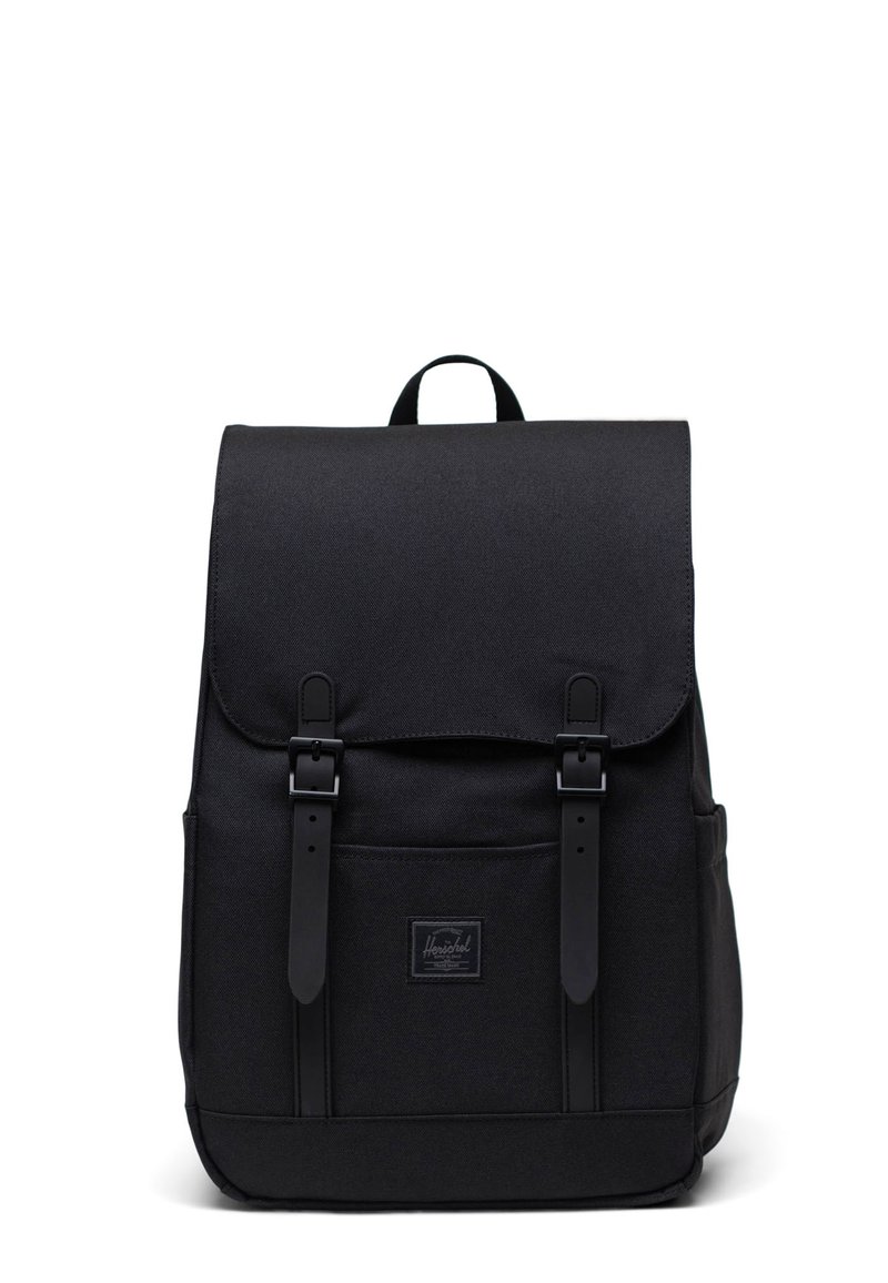 Zaino nero con tessuto texture, patta superiore, due cinturini con fibbia e una tasca frontale. Presenta un patch con logo vicino alla base.