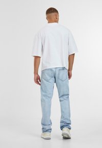 T-shirt blanche à manches courtes associée à un jean en denim bleu clair. Le T-shirt a une coupe droite ; le jean présente deux poches arrière avec des coutures.