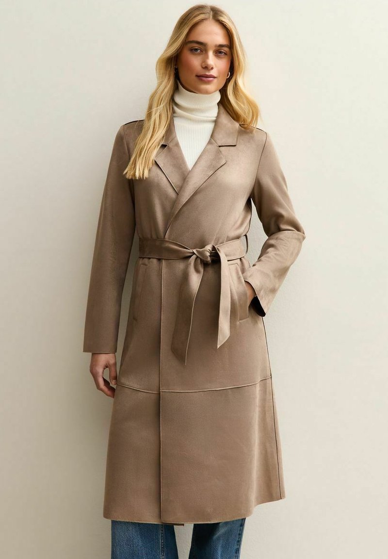 Bruine trenchcoat met riem gemaakt van gladde stof; heeft een reverskraag, lange mouwen en een knie-lange lengte. Gedragen over een trui.