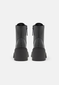 Bottes noires en cuir avec talons compensés épais et fermetures éclair à l'arrière, vues de dos sur un fond blanc uni.