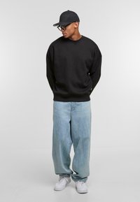 Schwarzer übergroßer Sweater, hellblaue baggy Jeans, weiße Sneakers und eine schwarze Kappe. Schlichte Gestaltung, weicher Stoff und lockere Passform.