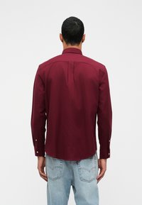 Bordo majica dugih rukava s glatkom teksturom, s klasičnom ovratnikom i zastavicama dugmadi, nosi se s svijetloplavim trapericama.