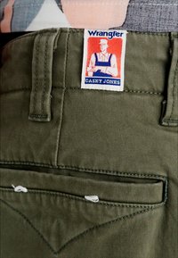 Olivgrüne Baumwollhosen mit einer Gesäßtasche und einem Wrangler "Casey Jones"-Etikett. Genähte Akzente und strukturiertes Material.