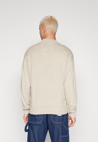 Jersey de manga larga beige con cuello redondo, tejido texturizado y puños de canalé. Combinado con pantalones cargo de mezclilla azul oscuro.