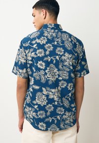 Camicia a maniche corte in tessuto blu con stampa floreale bianca; taglio comodo con colletto classico e texture sottile.