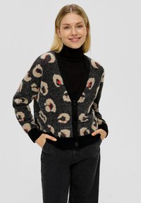 Zwart- en crèmekleurig luipaardprint cardigan met een V-hals, knopen aan de voorkant en geribbelde manchetten, gedragen over een zwarte coltrui. Zachte, gestructureerde stof.