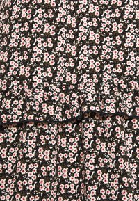 Černá tkanina s květinovým vzorem, obsahující malé bílé a růžové květy, doplněné zelenými listy. Detail volánového lemování.