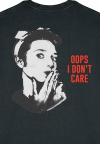 Zwarte T-shirt met een zwart-wit grafiek van een persoon met een vinger op de lippen en rode tekst die zegt "OOPS, I DON'T CARE."