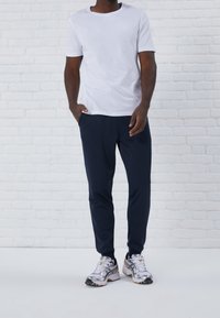 Vit t-shirt med kort ärm, marinblå träningsbyxor och silversneakers med svarta detaljer. Slätt tyg, avslappnad passform och enkel design.