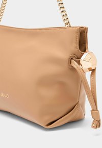 Beige leren handtas met een gladde textuur, kettingband en een geometrisch accent aan de zijkant. Voorzien van branding in metallic letters.