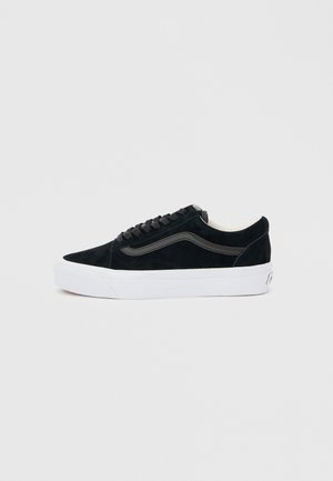 Schwarzer Sneaker mit niedrigem Schaft, schwarzen Schnürsenkeln, schwarzem Seitenstreifen und dicker weißer Sohle auf hellem grauem Hintergrund.