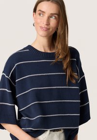 Pulover tricotat bleumarin cu dungi orizontale albe, guler și manșete cu nervuri și un design lejer. Textură netedă; stil casual.