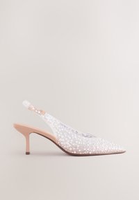 Chaussure beige à talon kitten avec bride arrière, bout pointu, recouverte de perles blanches décoratives et de perles.