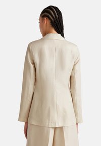 Beige, přizpůsobený blazer z lehkého materiálu; má klopový límec, dlouhé rukávy a bezešvý design zadní části s jemnou texturou.