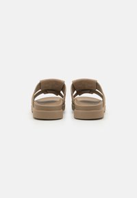 Sandales brunes avec un dessus en daim doux, arrière ouvert et larges sangles. Le design présente une semelle épaisse et confortable avec un matériel minimal.