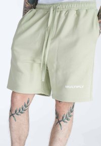 Pantaloni corti in cotone verde chiaro con vita elastica e cordoncino, con logo bianco "MULTIPLY" sulla gamba sinistra.