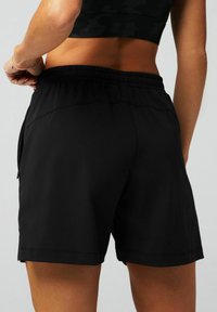 Schwarze Sportshorts aus leichtem Stoff. Verfügen über einen elastischen Bund und eine seitliche Reißverschlusstasche. Glatte Textur und reguläre Passform.