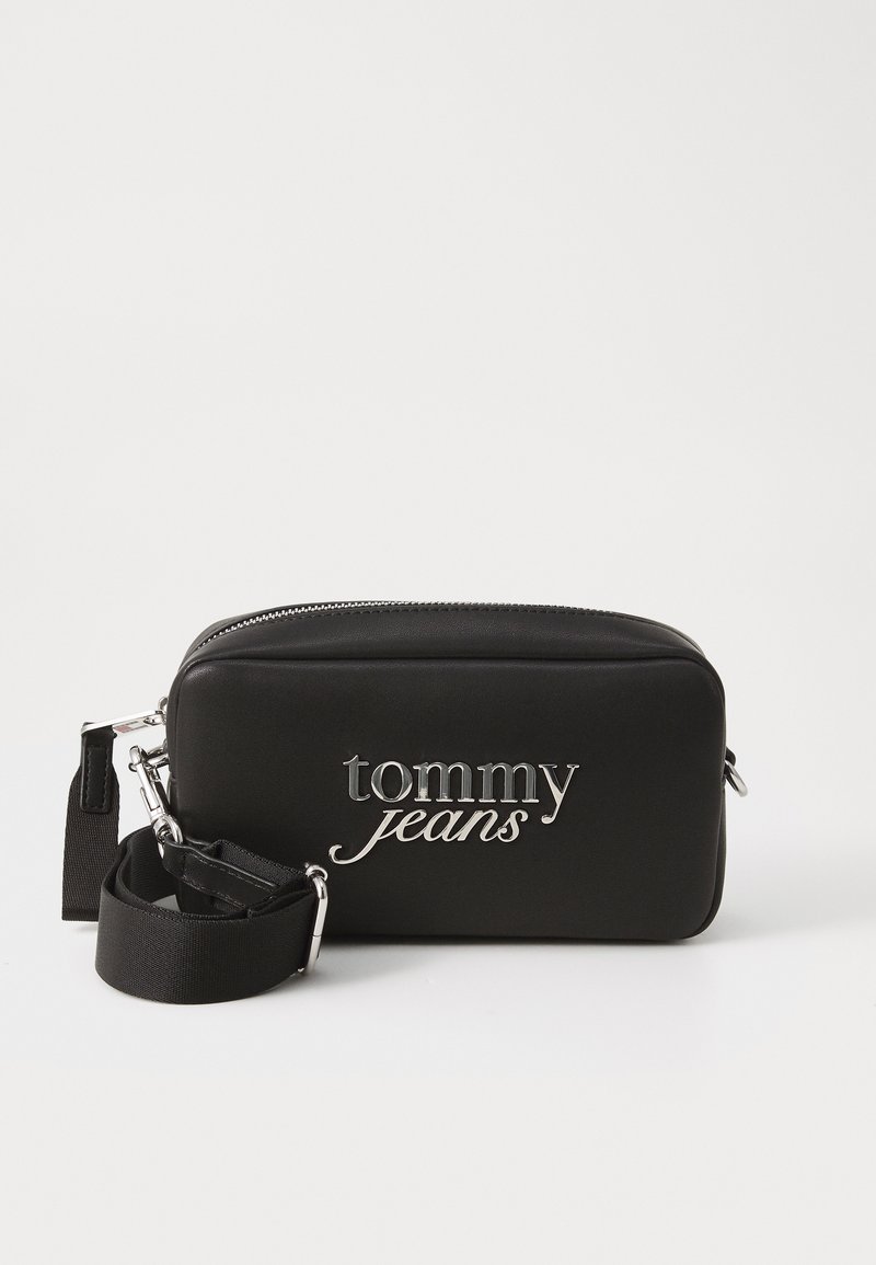 Juodas sintetinės medžiagos šalinis krepšys su sidabriniu "tommy jeans" logotipu, užtrauktukas, reguliuojama petneša. Lygus tekstūros paviršius, stačiakampio forma, kompaktiškas dizainas.