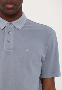 Light blue polo shirt made of textured fabric, featuring a three-button placket and a small embroidered logo on the left chest.