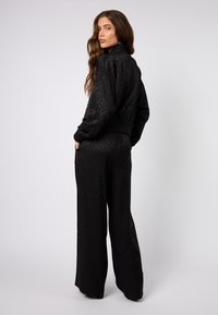 Czarny satynowy dres z panterkowym wzorem, składający się z kurtki w stylu bomber i szerokich spodni. Z detalami w postaci ściągaczy na mankietach i w pasie.