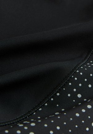 Sort stof med en glat tekstur, der har en mønstersektion med sølvprikker på en mørk baggrund, og kontrasterende sømdetaljer.