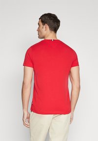 Rød t-shirt med korte ærmer lavet af bomuld. Har en rund halsudskæring, en trekantet detalje på ryggen og sidekantdetaljer i blå og hvid.
