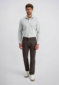 Helles blaues Hemd mit langen Ärmeln, kombiniert mit dunkelgrauen Hosen und weißen Sneakern. Sauberes Design, taillierte Form.